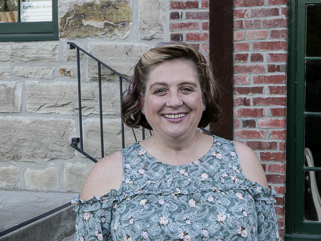 A smiling woman with short blond hair in a floral cold shoulder top.