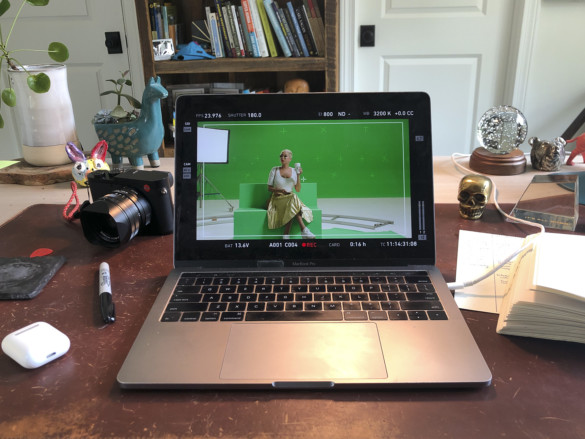 An open Mac Book with its screen showing an actress against a green screen.