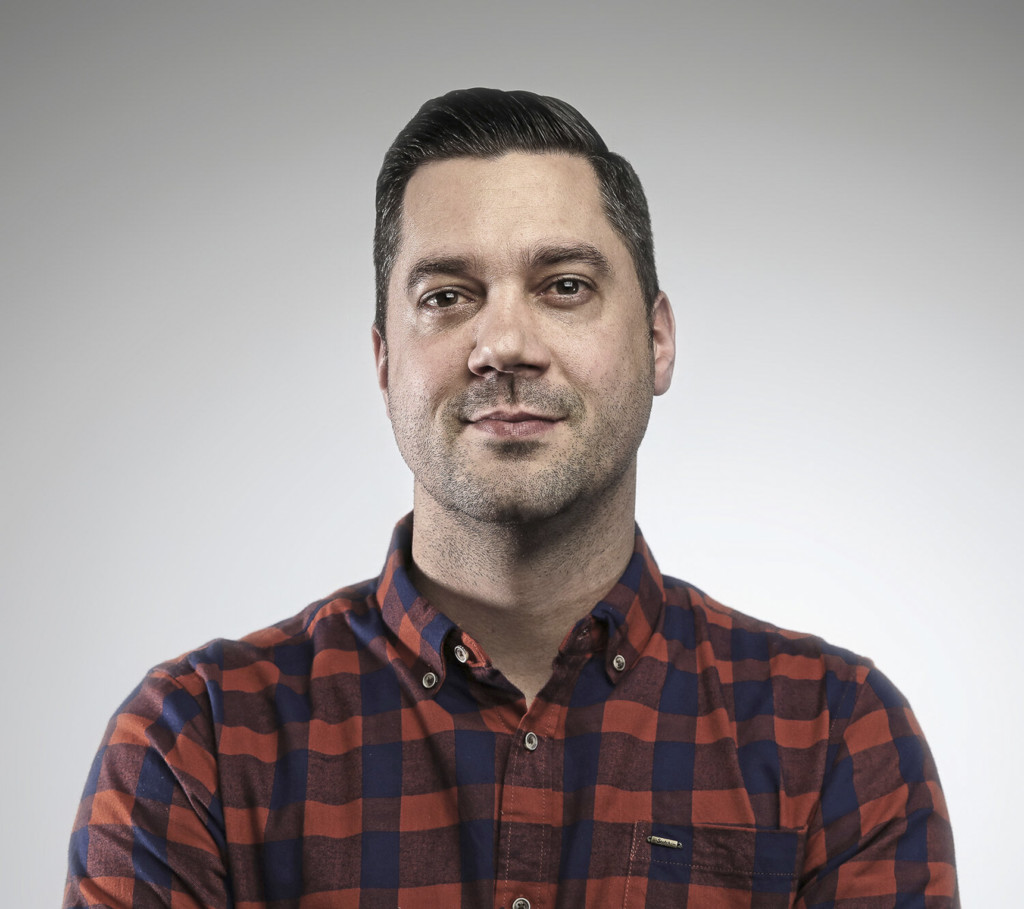 Advertising alumnus Jared Kozel wearing a red and black checked button down against a light gray background.